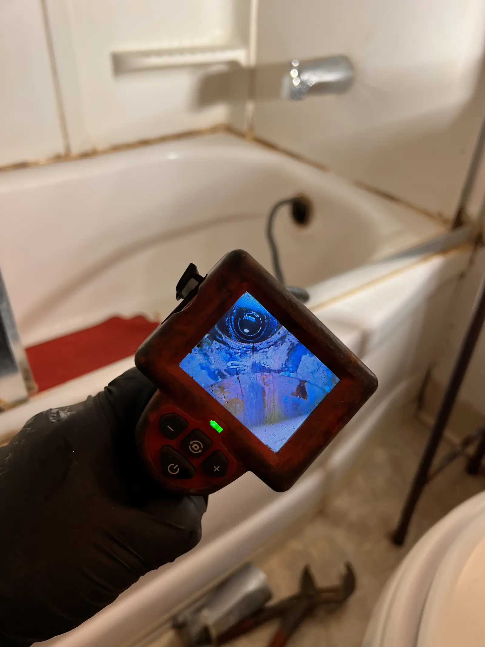 A hand holding a camera inspection monitor in a bathtub showing the inside of a drain line
