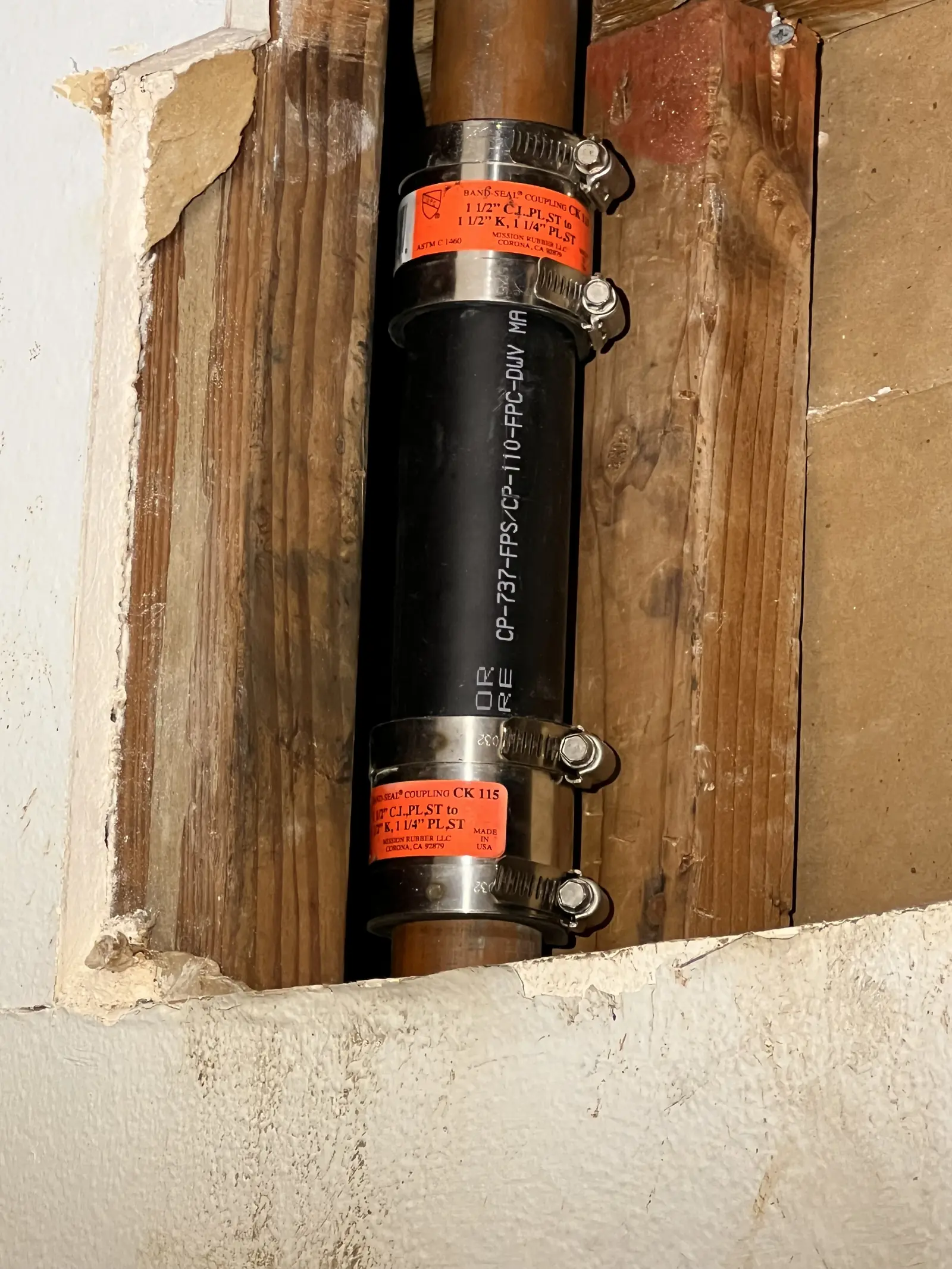 A cast iron drain stack in an opened wall with two black no-hub couplings