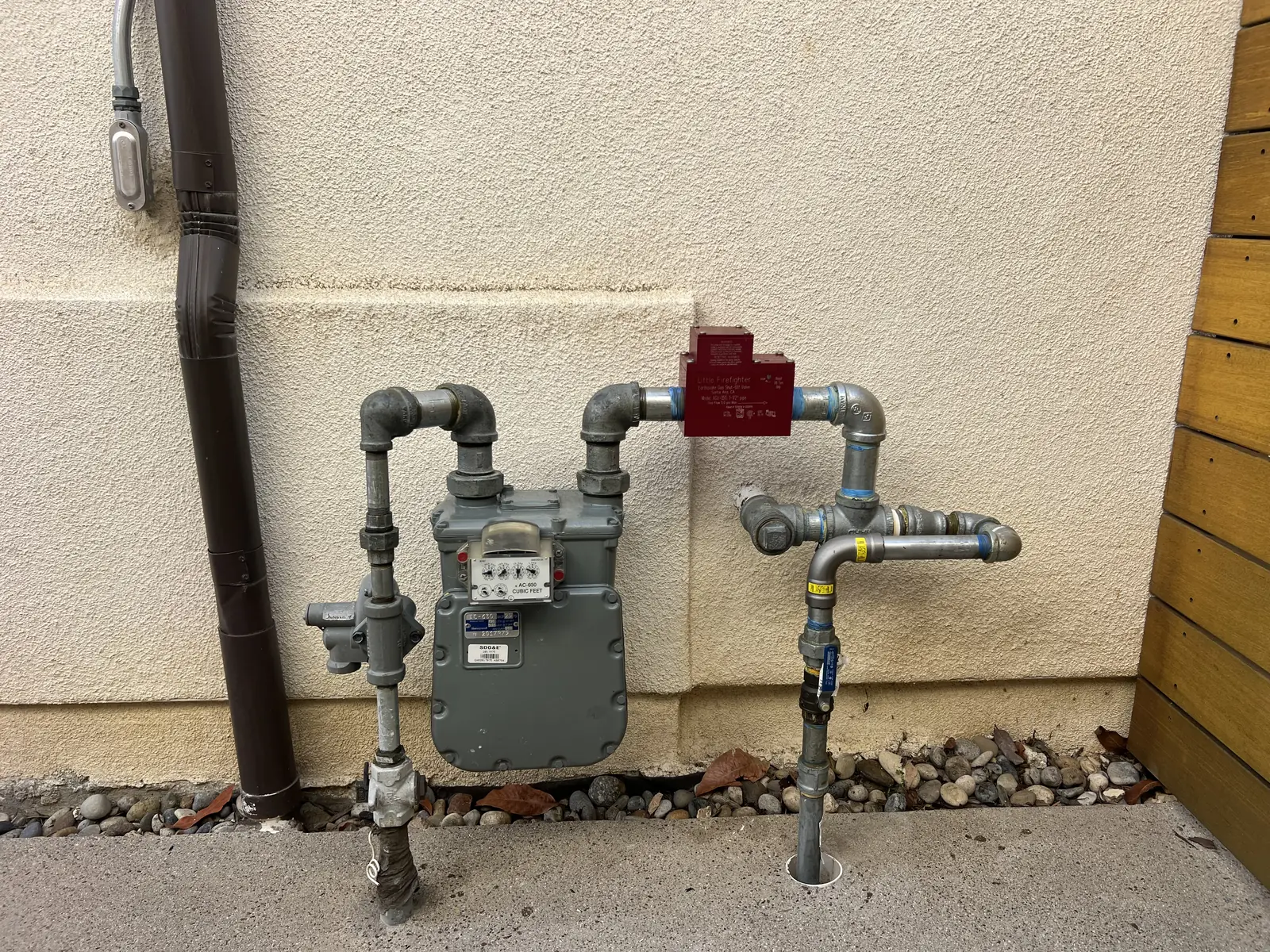 A gas meter and its pipe riser on the outside wall of a house