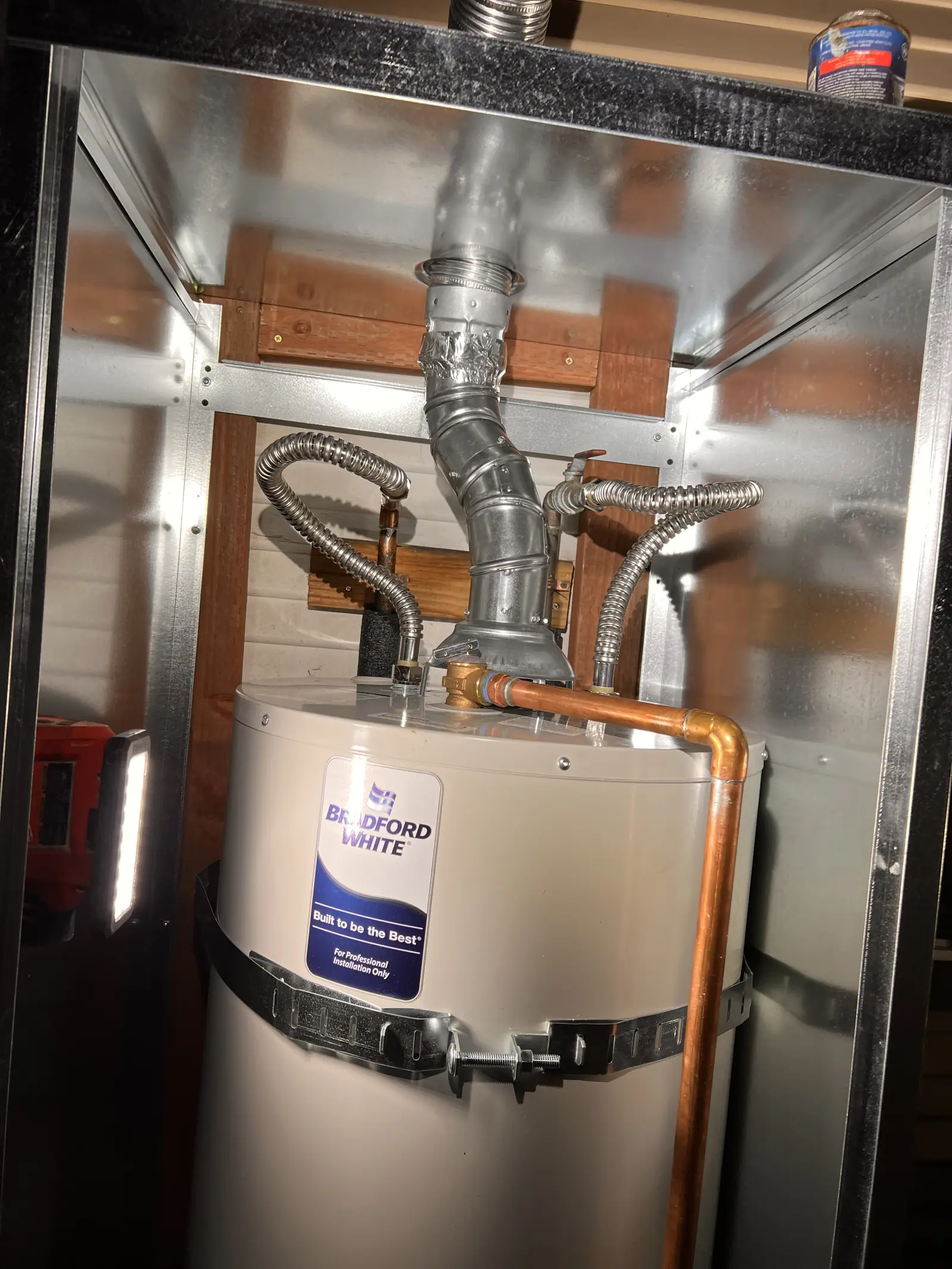 A large Bradford White water heater in a stainless steel enclosure with vent and copper lines