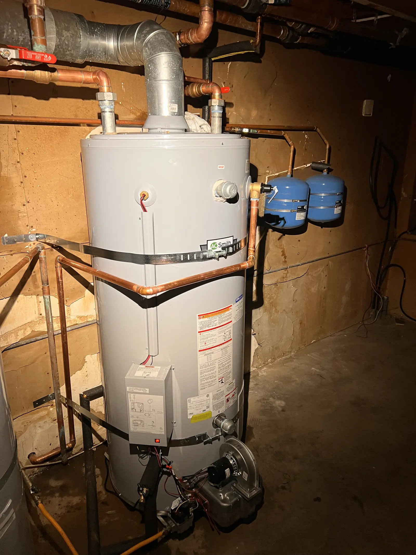A tank water heater with two blue expansion tanks, a vent and copper piping