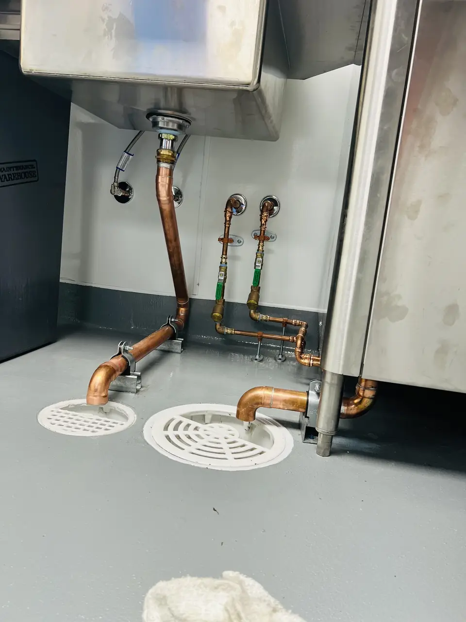 Copper waste lines under a stainless sink running to round floor drains