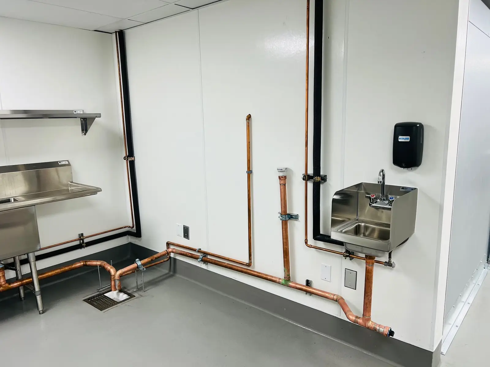A commercial kitchen room with copper lines along the walls to a hand sink and a three-compartment sink