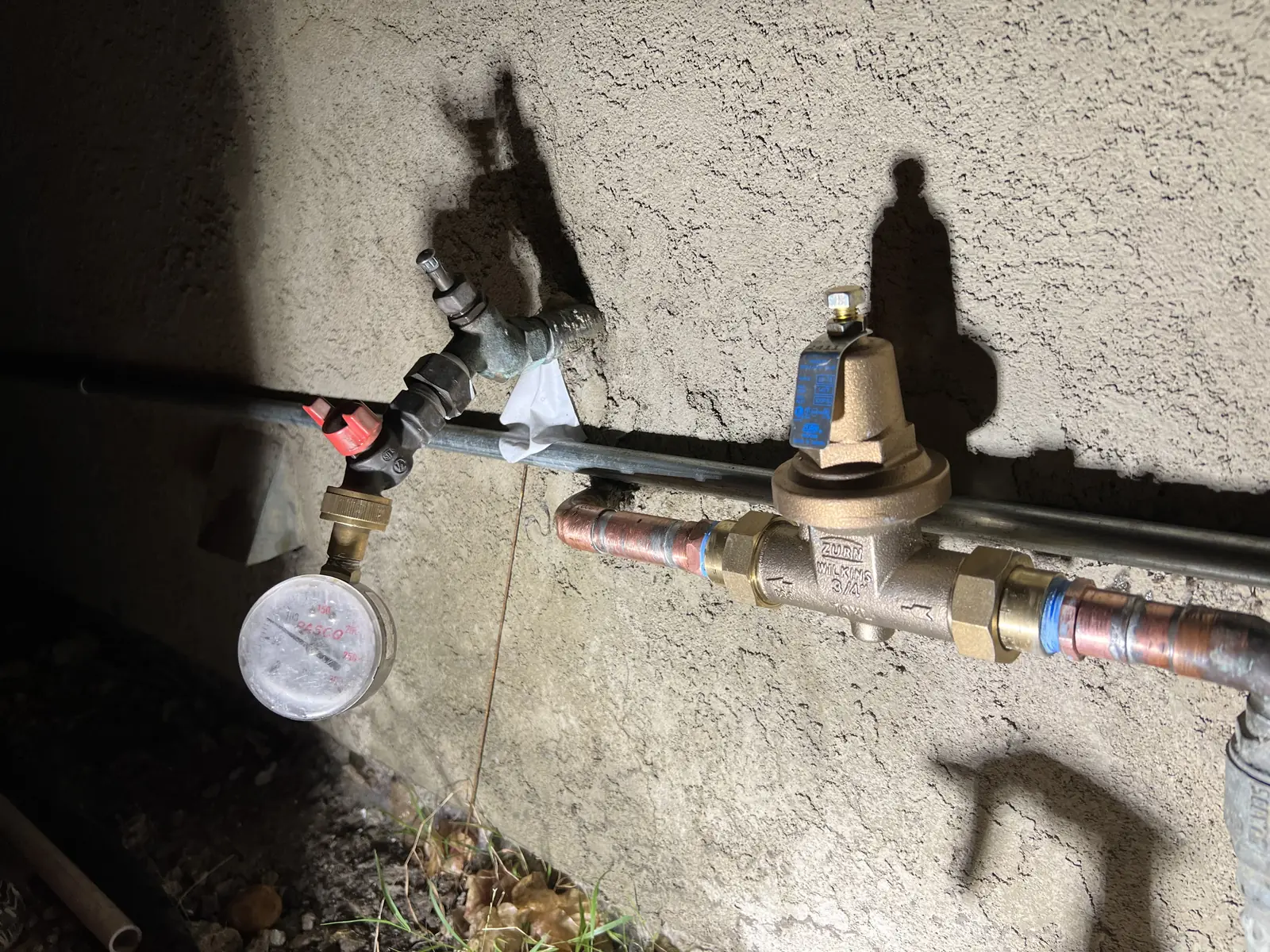 A pressure regulator valve with a pressure gauge on a water line at an outside wall