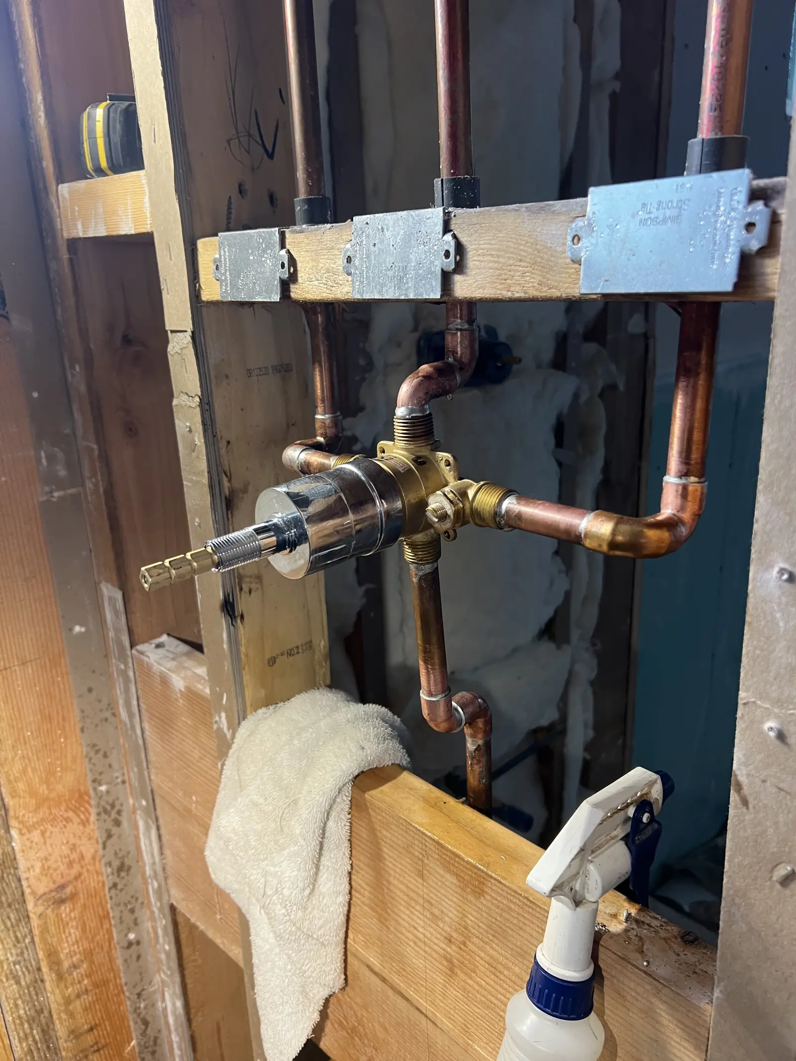 A shower valve with copper lines in an opened wall, a towel and spray bottle below