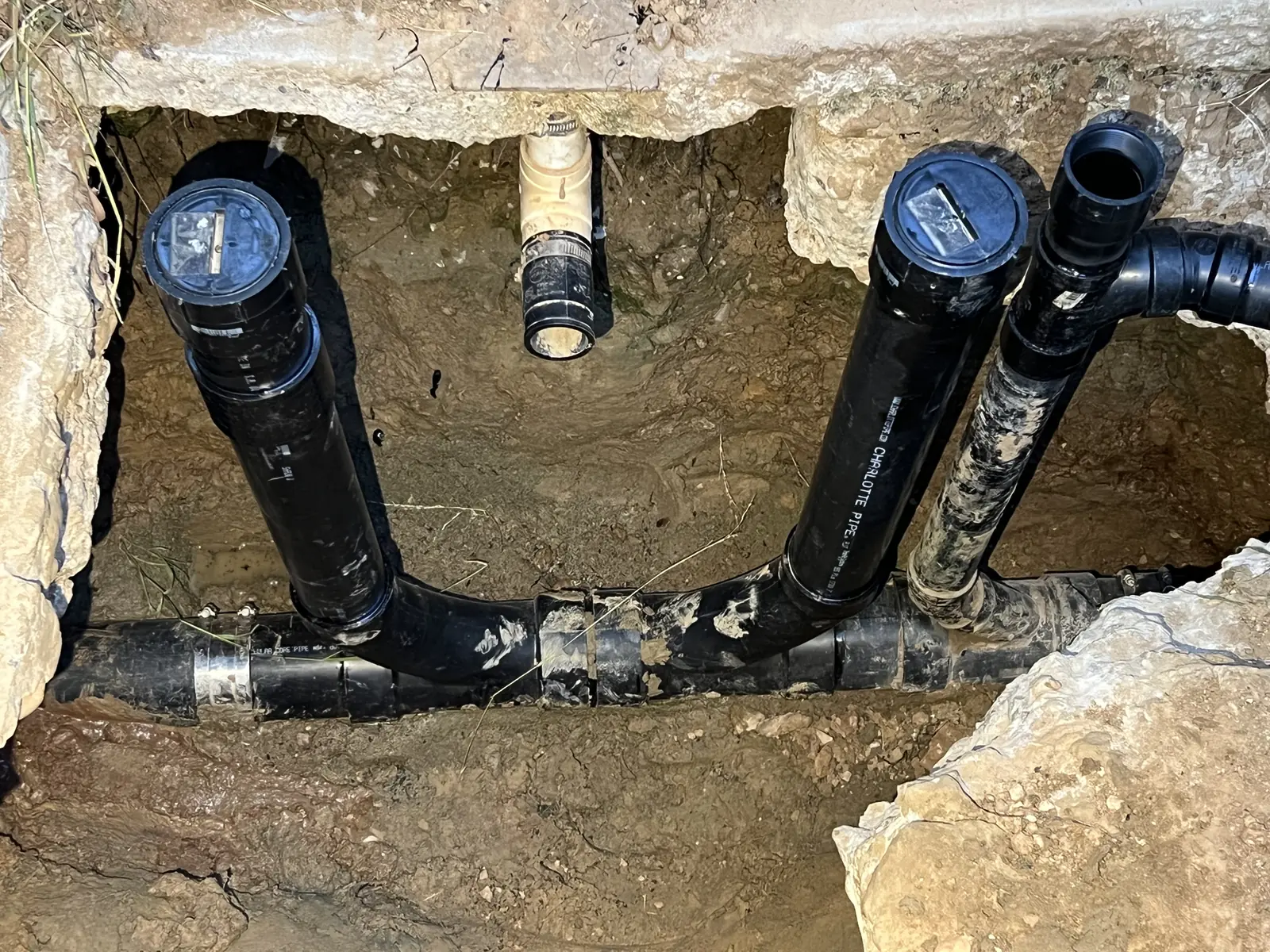A cut-open slab with black cast iron and ABS drain pipes and a tee below the floor