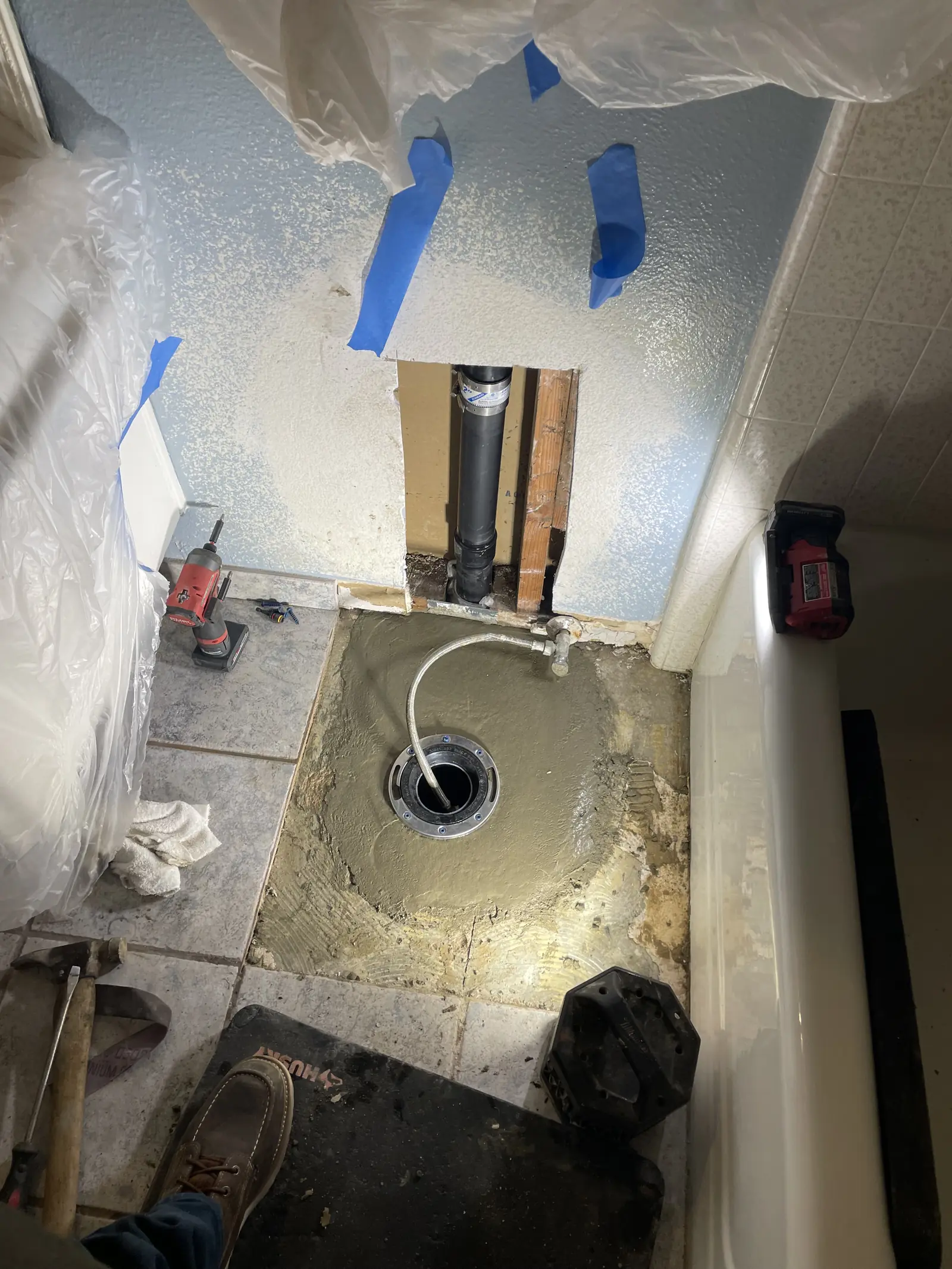 A bathroom floor opened to the dirt with a new drain pipe and tape marks on the wall