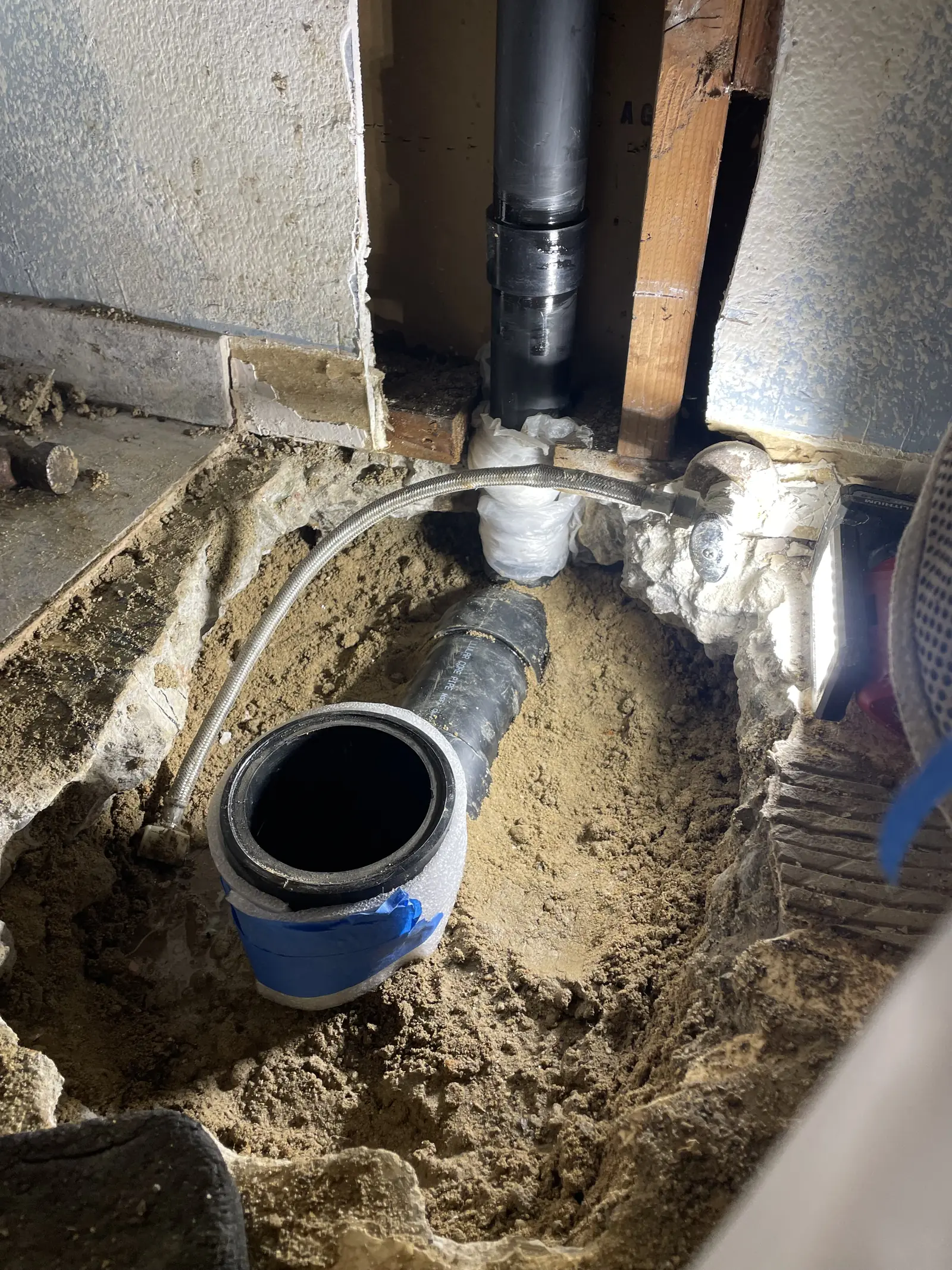 An excavated trench with a new black pipe, a cleanout and a coil of line beside it