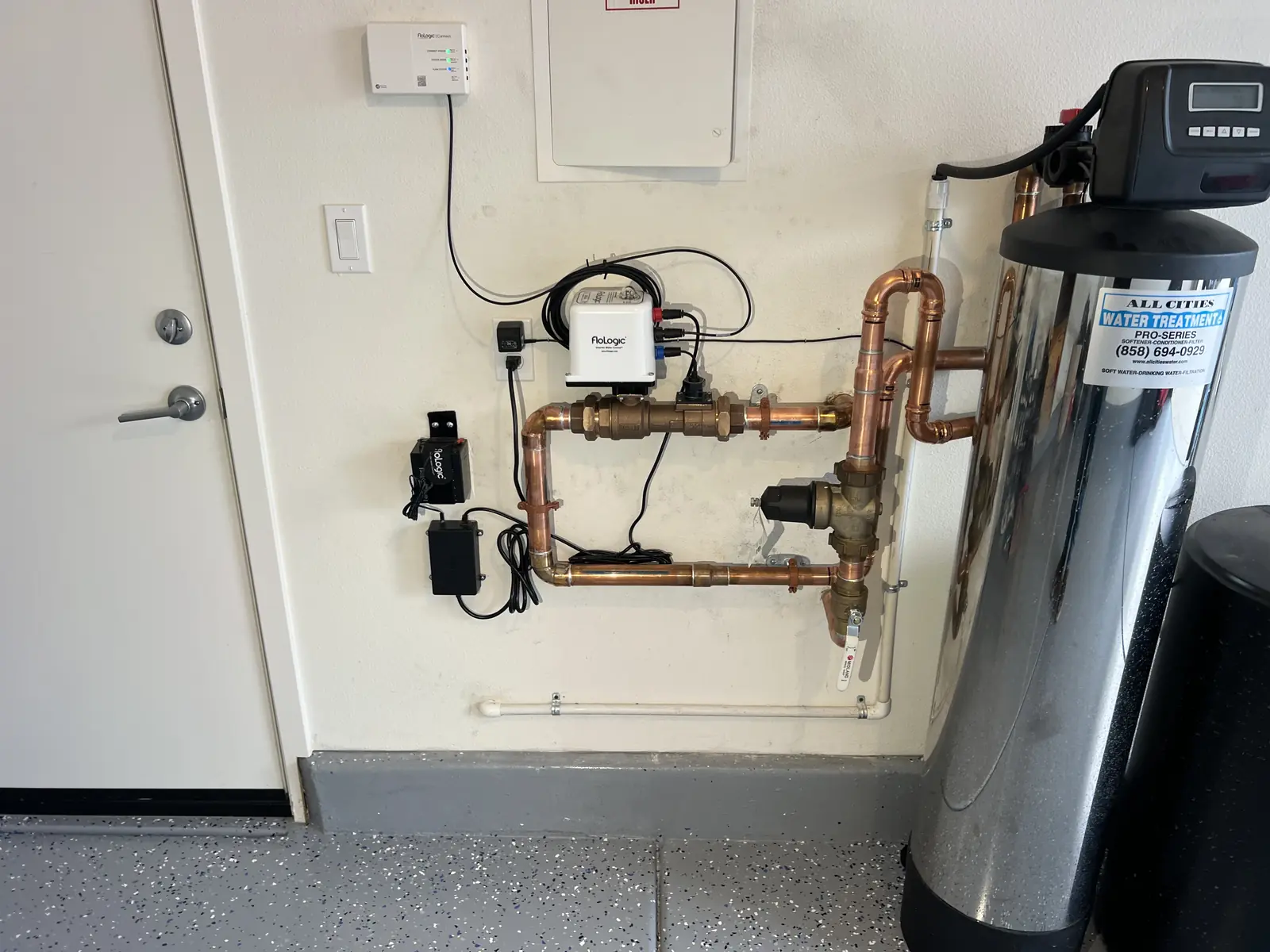 A water treatment tank with a copper manifold, valves and a control head on a garage wall