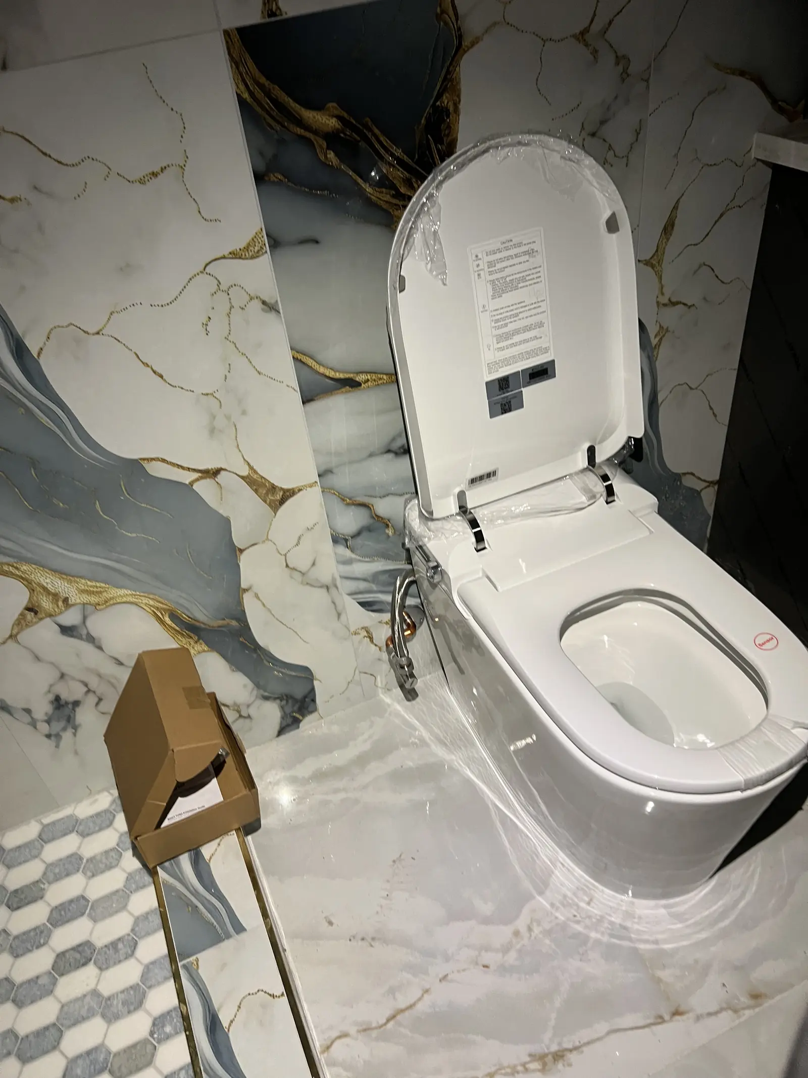 A new white toilet installed in a bathroom with marble-look tile