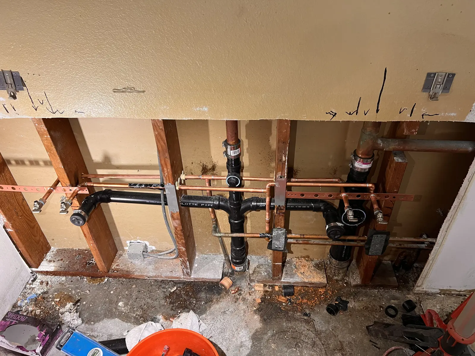 An opened wall with black drain pipe, fittings and copper lines before the wall is closed